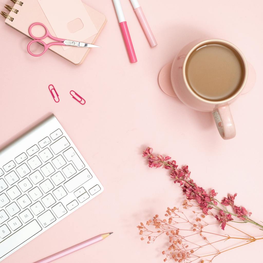 Aesthetic flat lay of a pink desk featuring stationery, coffee, and flowers for a modern workspace vibe.