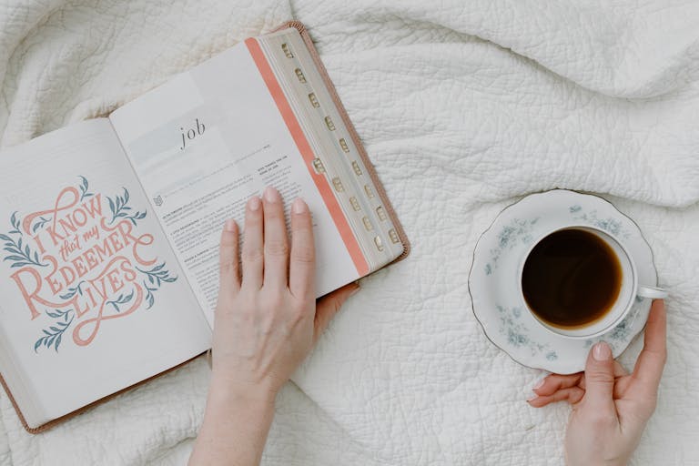 Top view of morning Bible study with coffee, featuring open Bible and feminine hands.