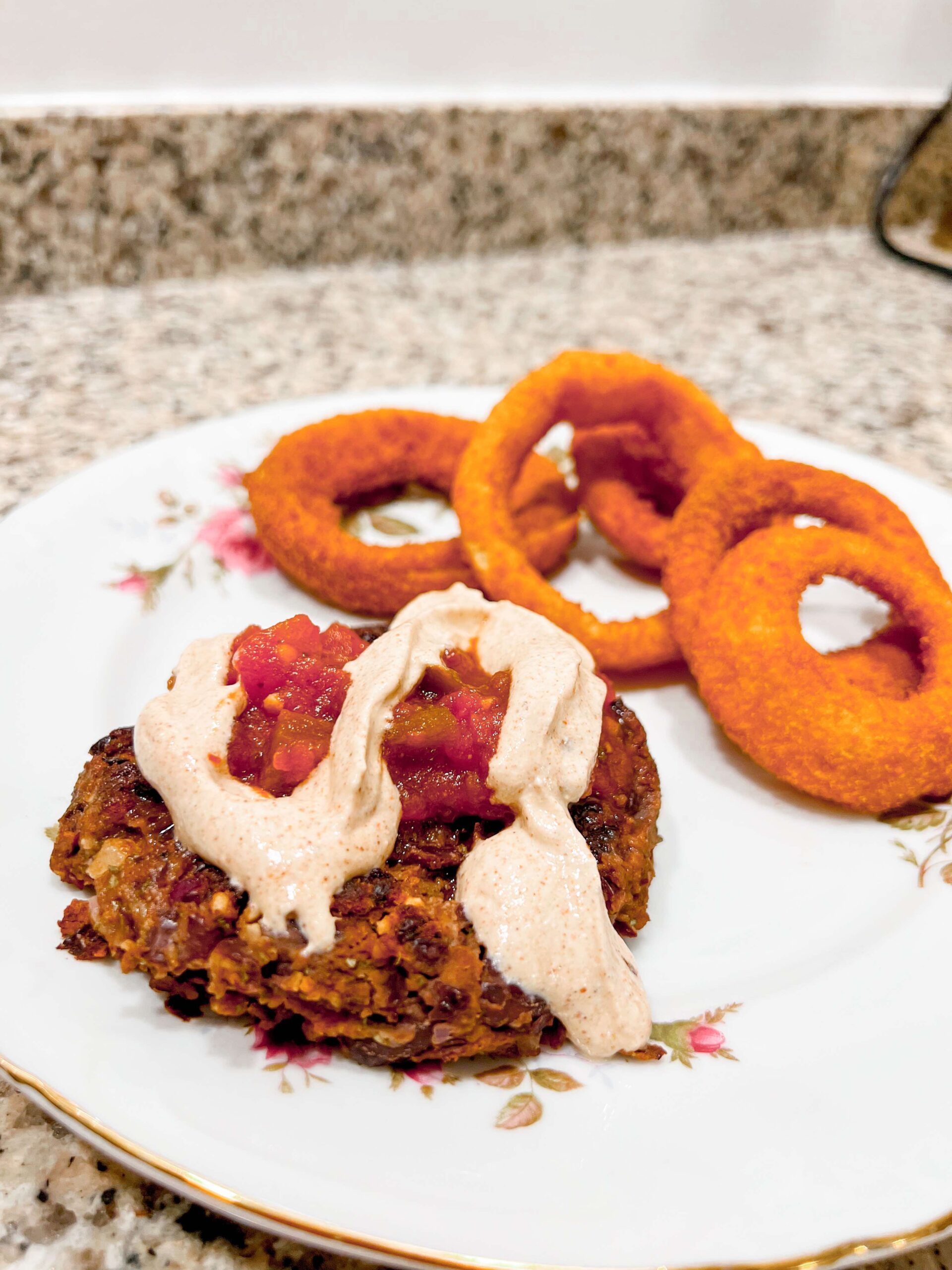 homemade black bean burger on a plate with onion rings